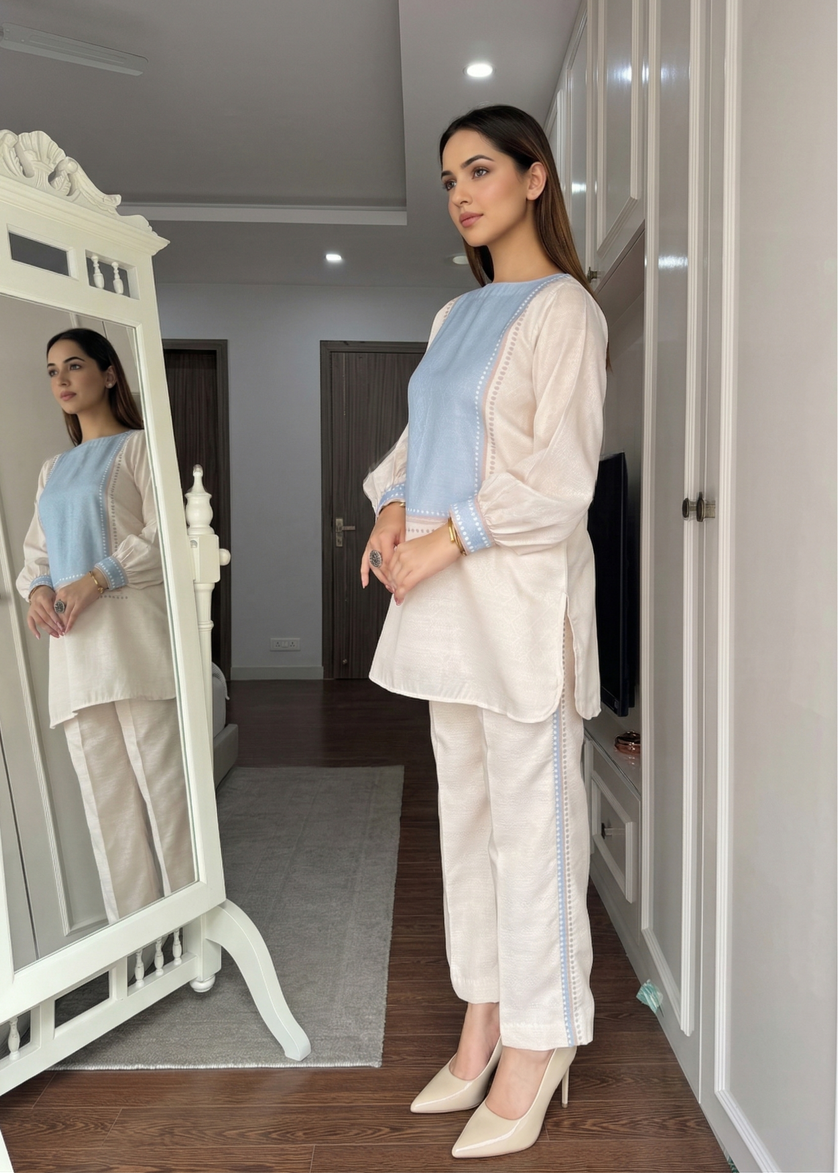 Woman standing in front of a mirror wearing a light-colored outfit with a blue vest.